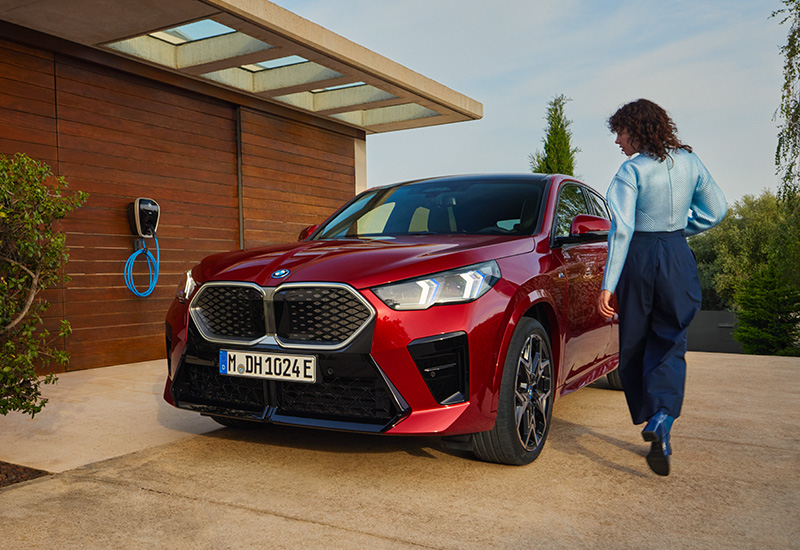 BMW iX2 Frontansicht, Frau steht neben Fahrzeug
