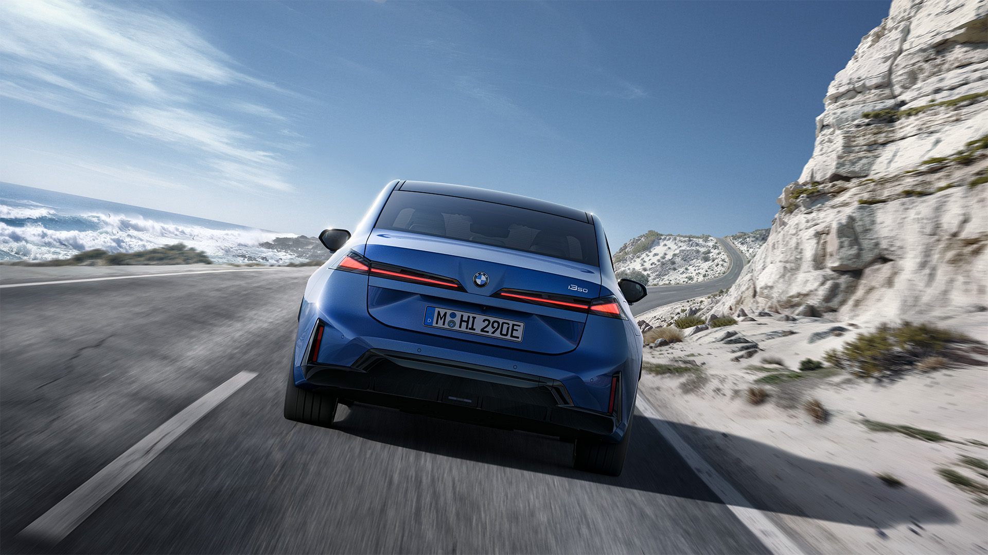 BMW i3 Limousine in Fahrt von hinten fotografiert mit Felsen und Meer im Hintergrund