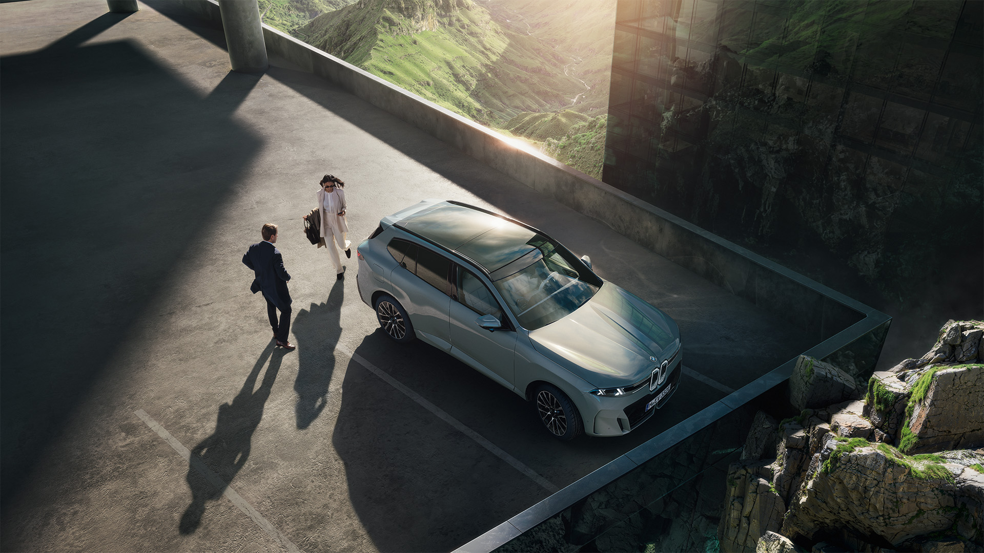 BMW iX5 (G65) in silbergrau stehend auf einem Parkdeck - fotografiert von oben mit Felsen im Hintergrund